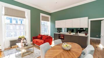 A modern living room with a red sofa, a round dining table, and a kitchen with white cabinets.