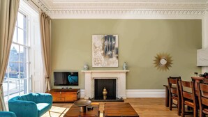 A living room with a fireplace, a television, and a dining area with wooden chairs. - Bell Suite - 2 Bed 2 Bath Luxury Apartment (Edinburgh)