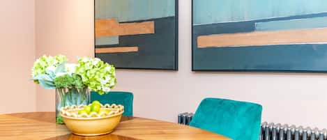 A modern dining area with a round wooden table, teal chairs, and a vase with green flowers.