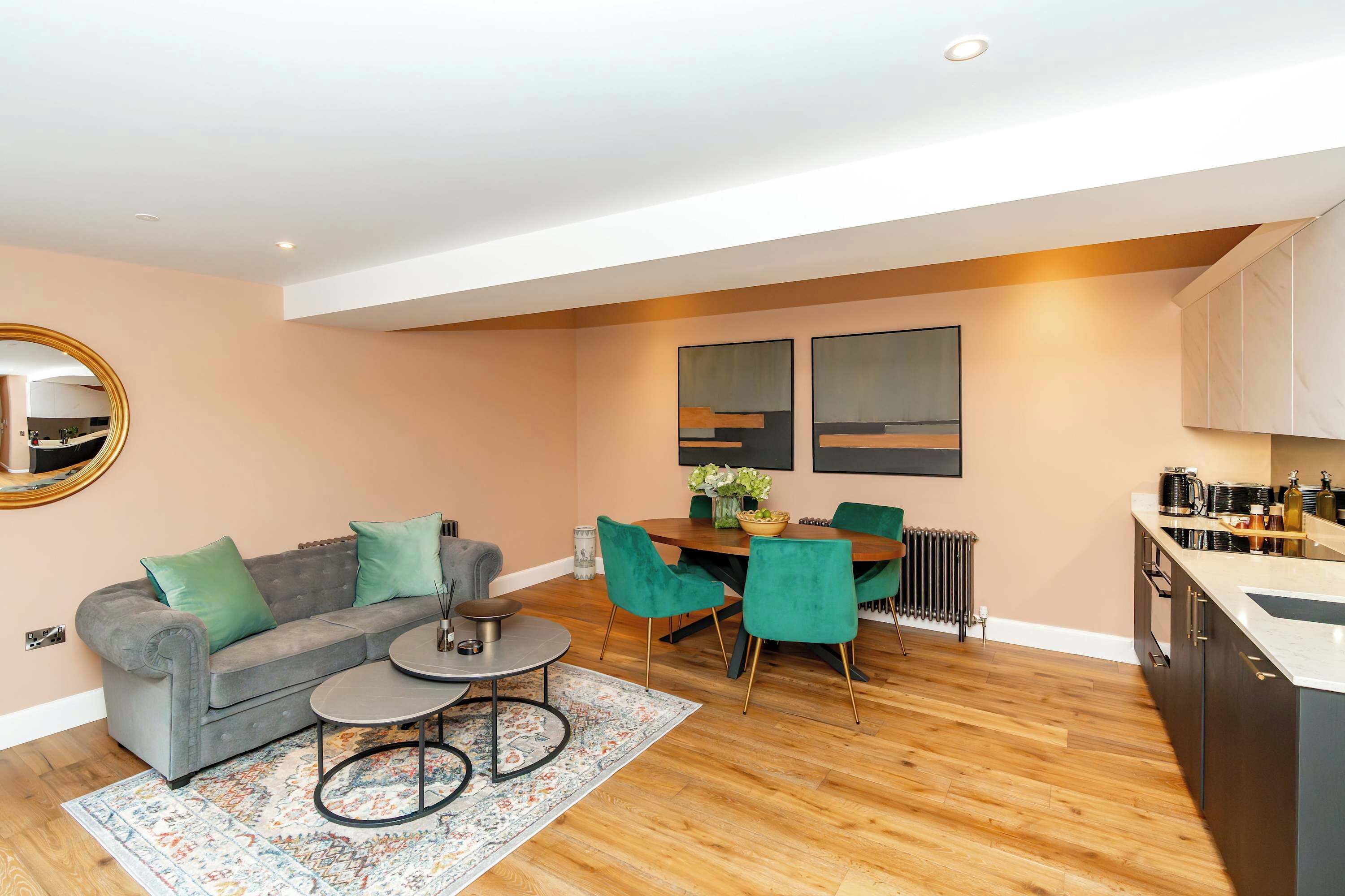 A modern living room with a grey sofa, a coffee table, and a dining area with a wooden table and green chairs.