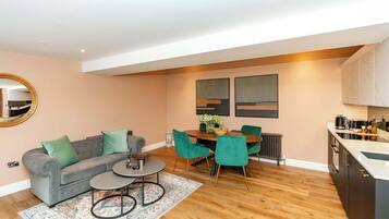 A modern living room with a grey sofa, a coffee table, and a dining area with a wooden table and green chairs.