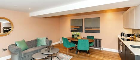 A modern living room with a grey sofa, a coffee table, and a dining area with a wooden table and green chairs.