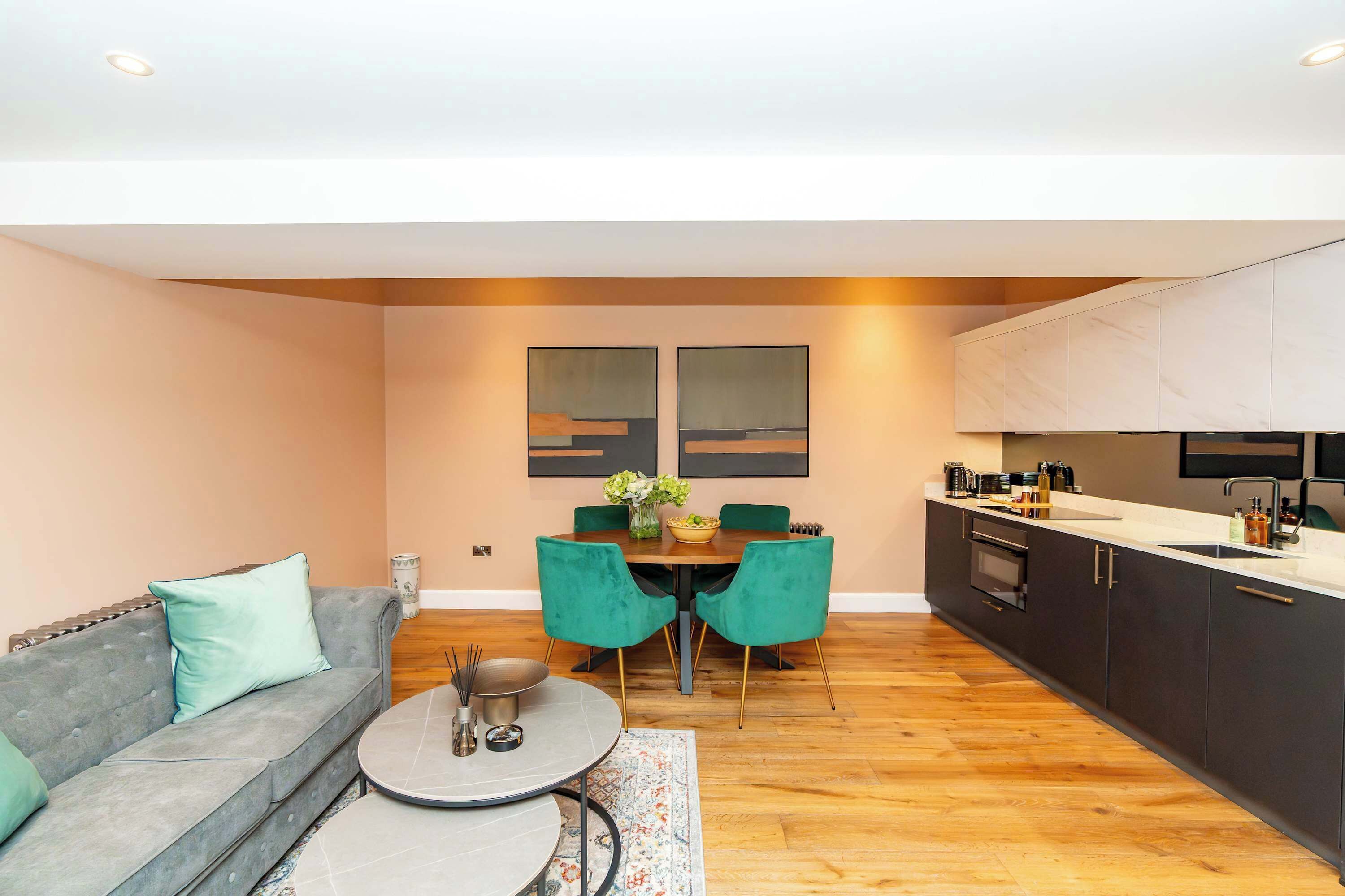 A modern living room with a grey sofa, teal chairs, a round coffee table, and a dining area with a wooden table and chairs.