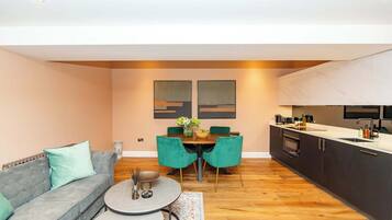 A modern living room with a grey sofa, teal chairs, a round coffee table, and a dining area with a wooden table and chairs.
