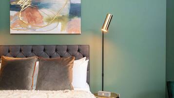 A bedroom with a tufted headboard, a bed with multiple pillows, a floor lamp, and a small table with a decorative item.