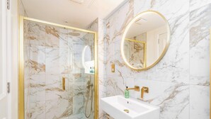 A bathroom with a glass-enclosed shower, a white sink with gold fixtures, and a marble-patterned wall. - Dragon Suites, Kerr Suite - 1 Bed Luxury Apartment (Edinburgh)