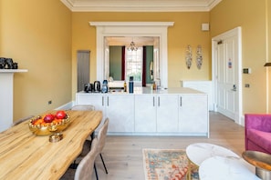 A modern kitchen with white cabinetry, a dining area with a wooden table and chairs, and a view into the adjacent bedroom. - 2 Bed Luxury Apartment (Edinburgh)
