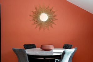 A dining area with a round table, four chairs, and a wall-mounted sunburst mirror. - Buchan Suite - 1 Bed Luxury Apartment (Edinburgh)