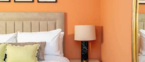 Un dormitorio con una cama, almohadas, una mesita de noche con lámpara y tres cuadros en la pared.