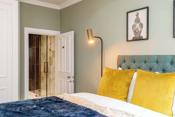 A bedroom with a bed, a bedside lamp, a door, and a framed picture on the wall. - Maxwell Suite - 1 Bed Luxury Apartment (Edinburgh)