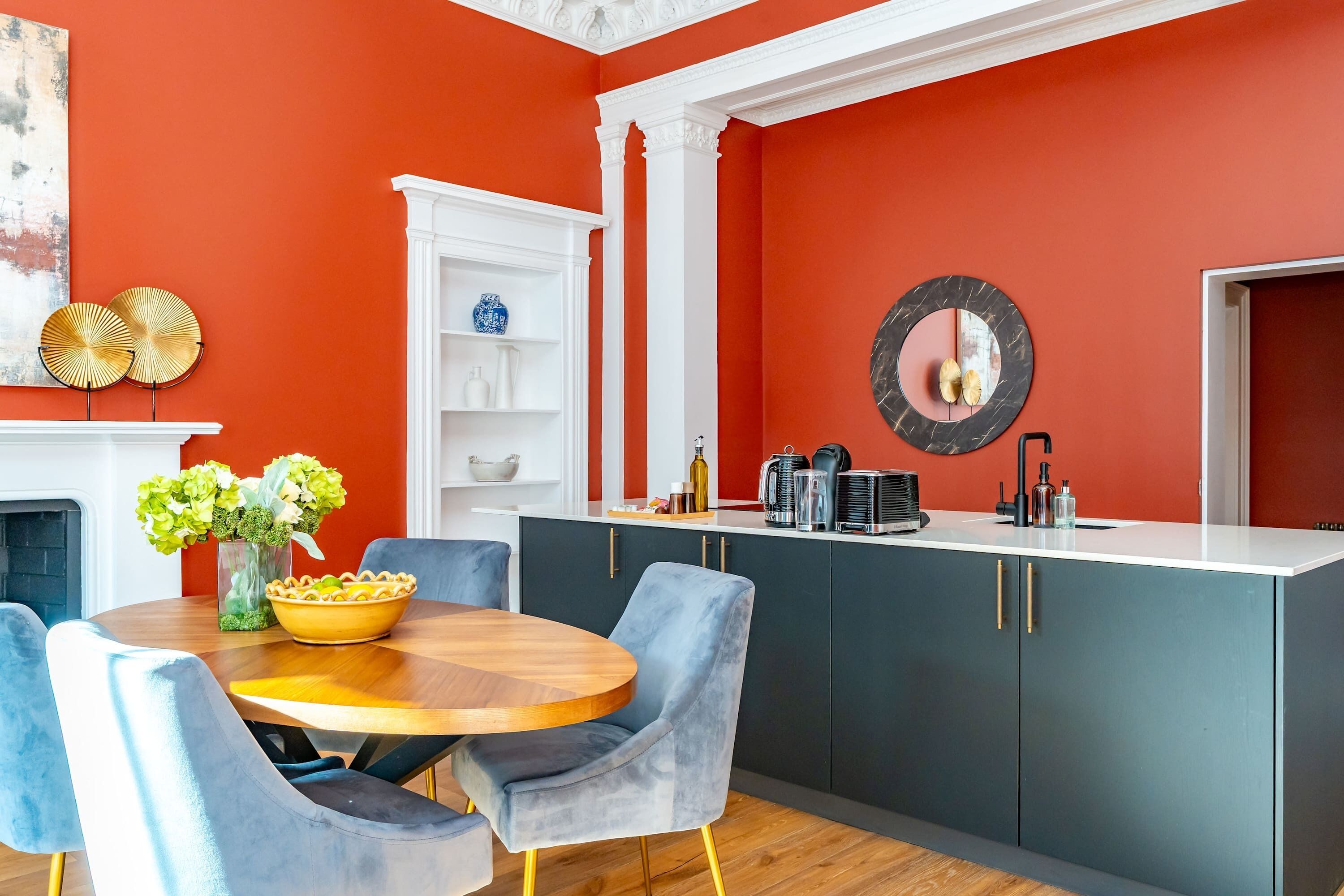 A modern kitchen with a red accent wall, a round dining table, and blue chairs.