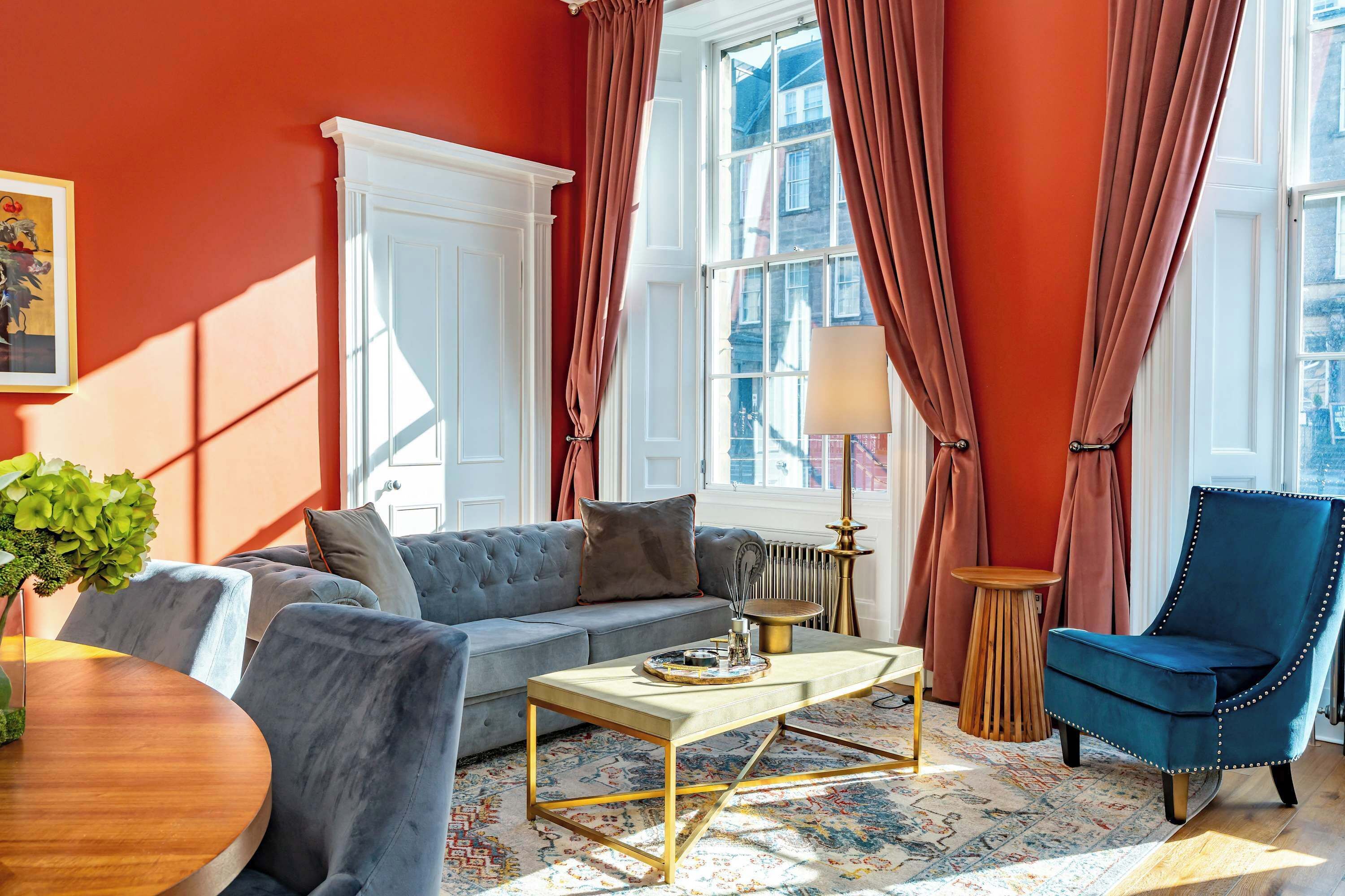 A living room with a sofa, armchair, coffee table, and a view of the city through large windows.