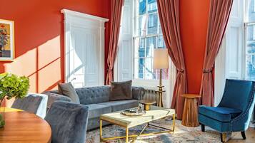 A living room with a sofa, armchair, coffee table, and a view of the city through large windows.