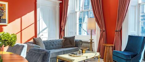 A living room with a sofa, armchair, coffee table, and a view of the city through large windows.