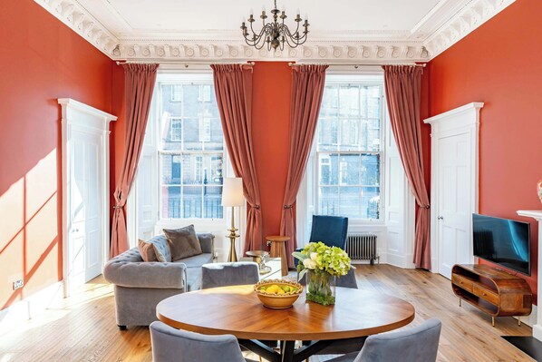 A room with a round wooden table, two sofas, a TV, and a window with curtains. - Swinton Suite - 1 Bed Luxury Apartment (Edinburgh)