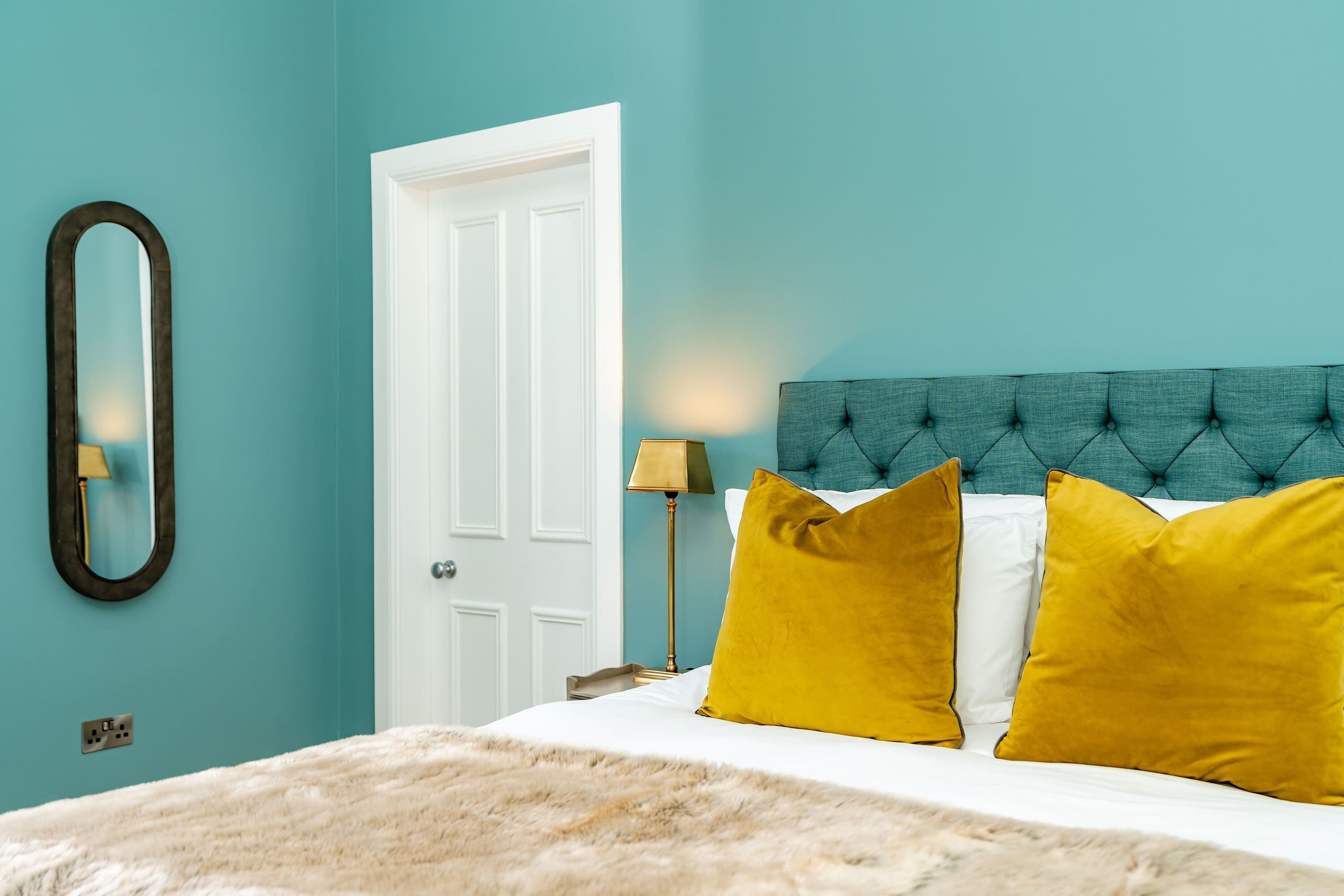 Een slaapkamer met een bed, een witte deur, een spiegel en een lamp.