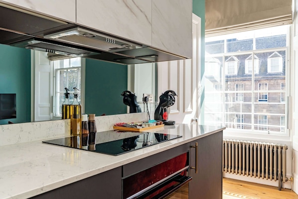 A modern kitchen with a large window, a built-in stove, and a mirror above the counter. - Gilmour Suite - 1 Bed Luxury Apartment (Edinburgh)