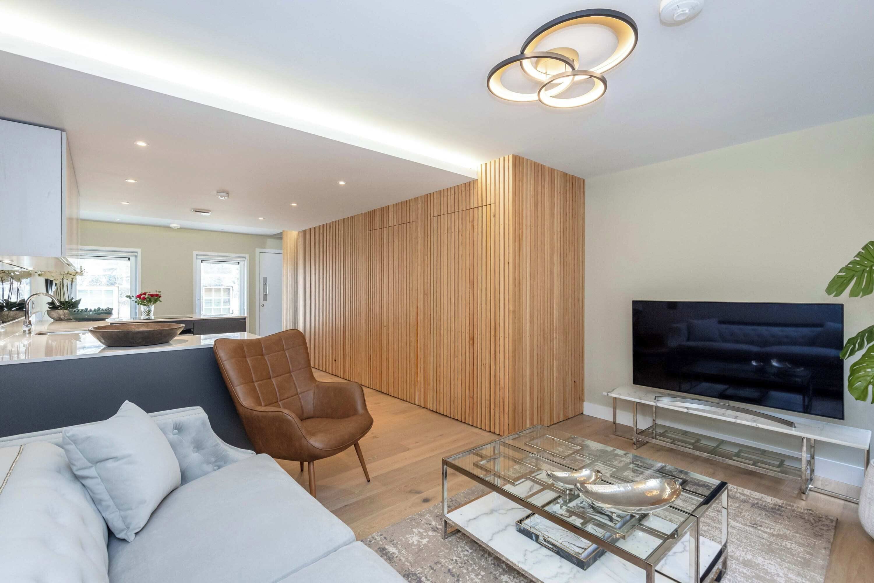 A modern living room with a sofa, a glass coffee table, a TV, and a wooden accent wall.