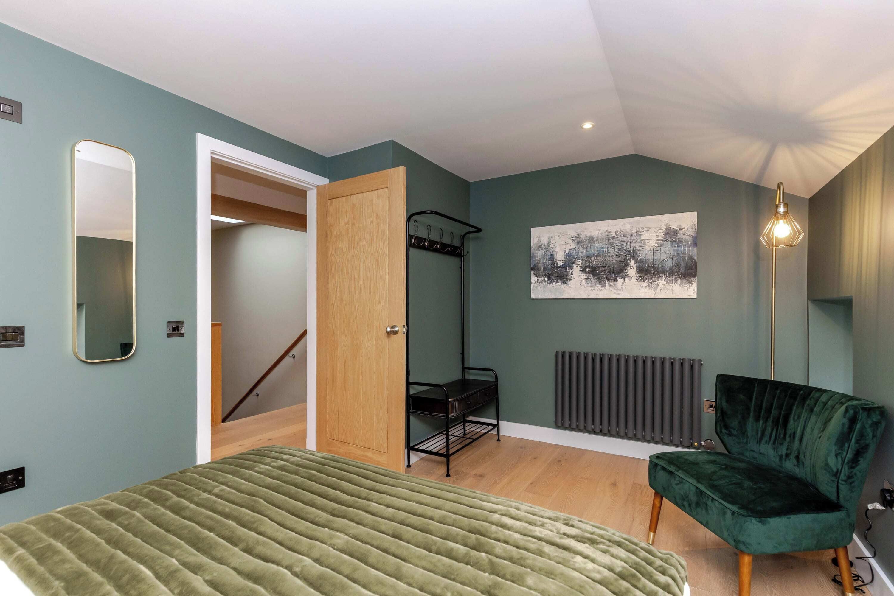 A bedroom with a bed, a chair, a radiator, a door, and a wall-mounted artwork.
