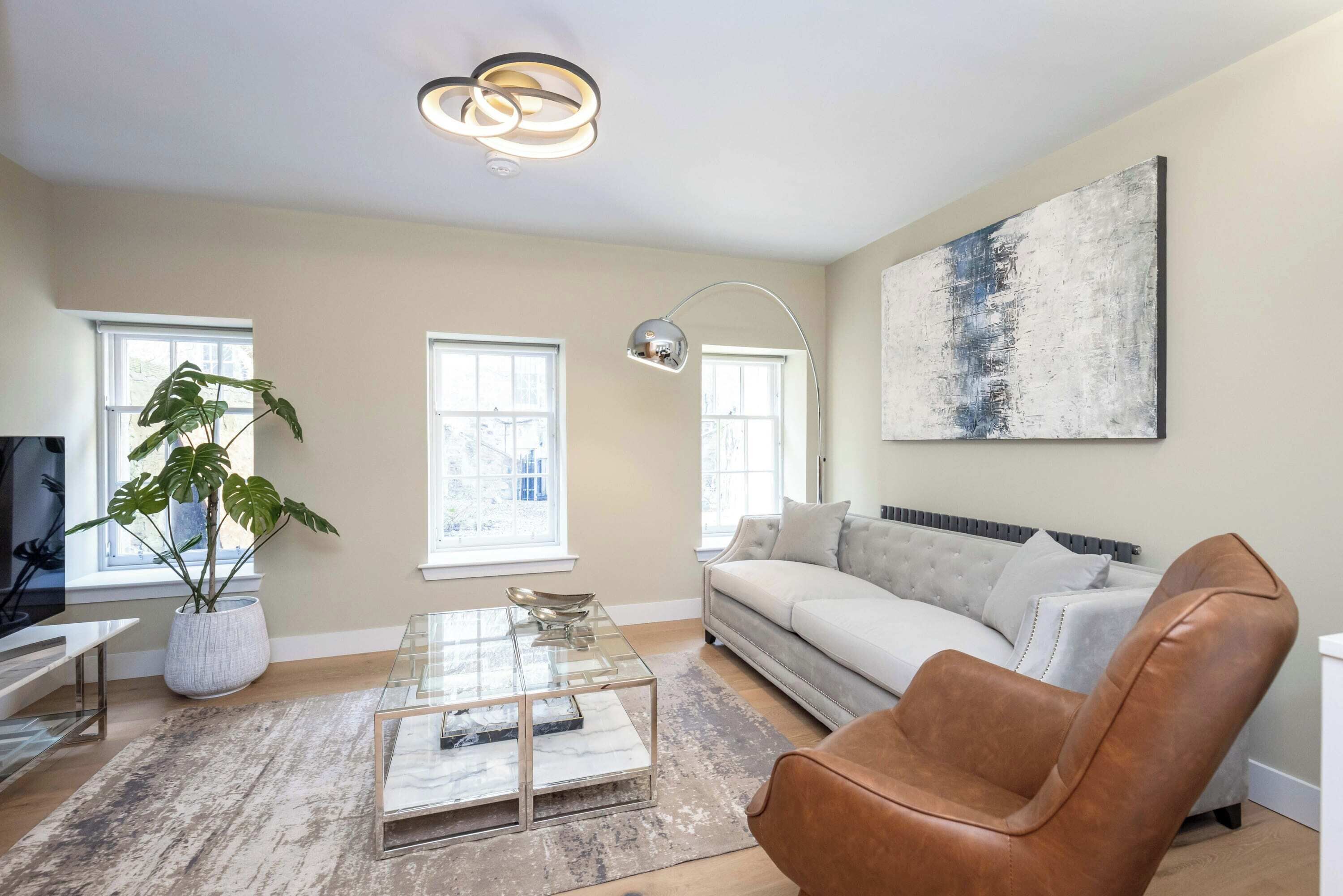 A modern living room with a sofa, a coffee table, a plant, and a painting on the wall.