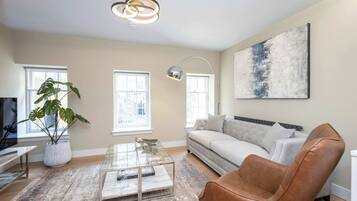 A modern living room with a sofa, a coffee table, a plant, and a painting on the wall.