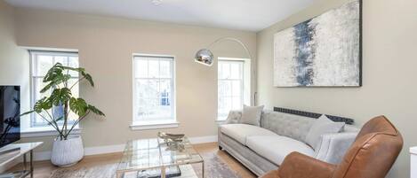 A modern living room with a sofa, a coffee table, a plant, and a painting on the wall.