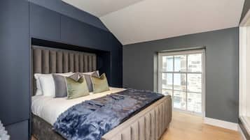 A modern bedroom with a large bed, a headboard, and a window with a view of buildings.