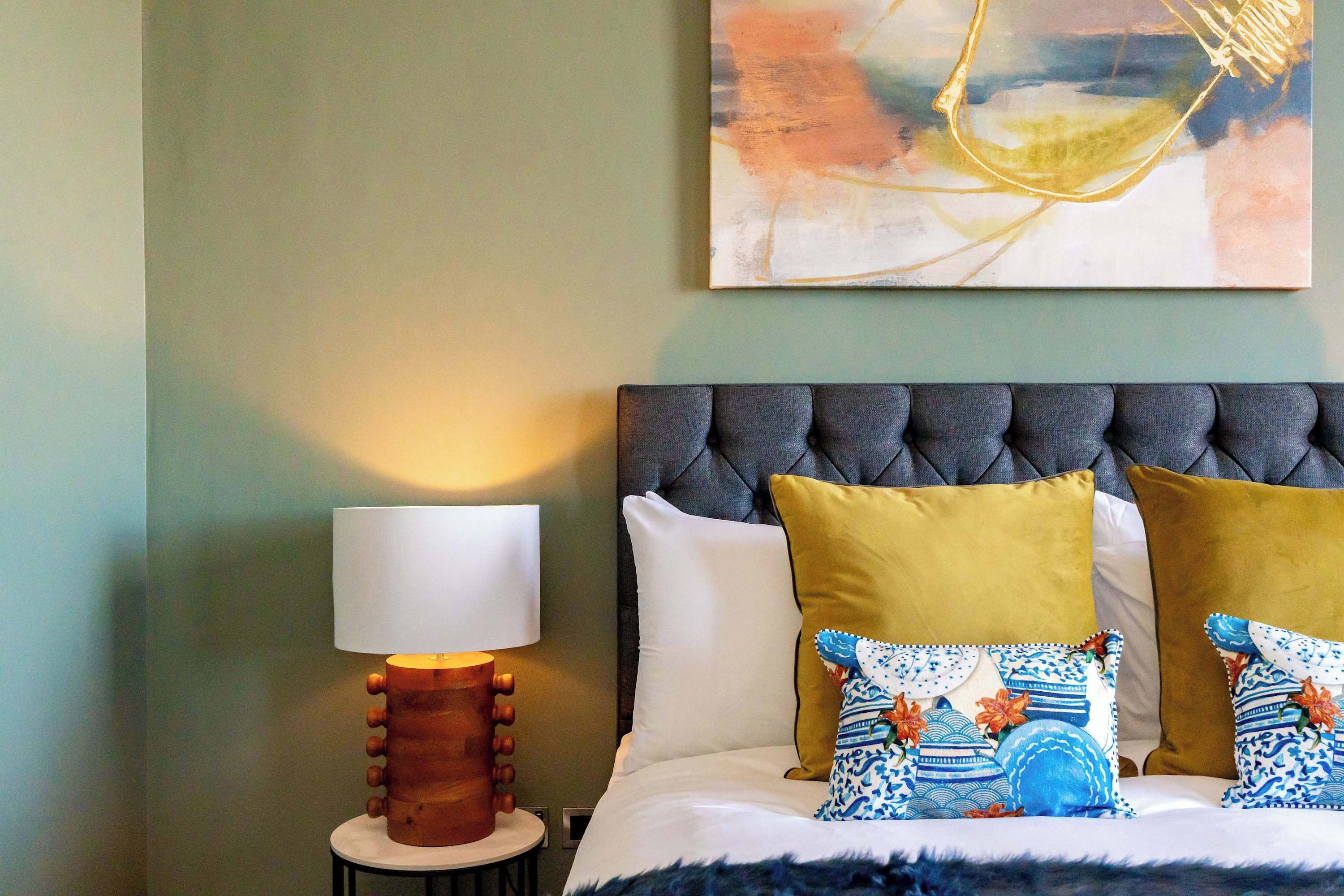 A neatly made bed with a tufted headboard, a bedside lamp, and decorative pillows.