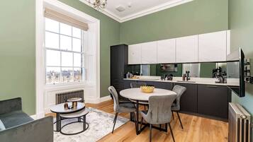 A modern kitchen with a round dining table, grey chairs, and a view through a large window.