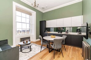 A modern kitchen with a round dining table, grey chairs, and a view through a large window. - Mackintosh Suite - 1 Bed Luxury Apartment (Edinburgh)