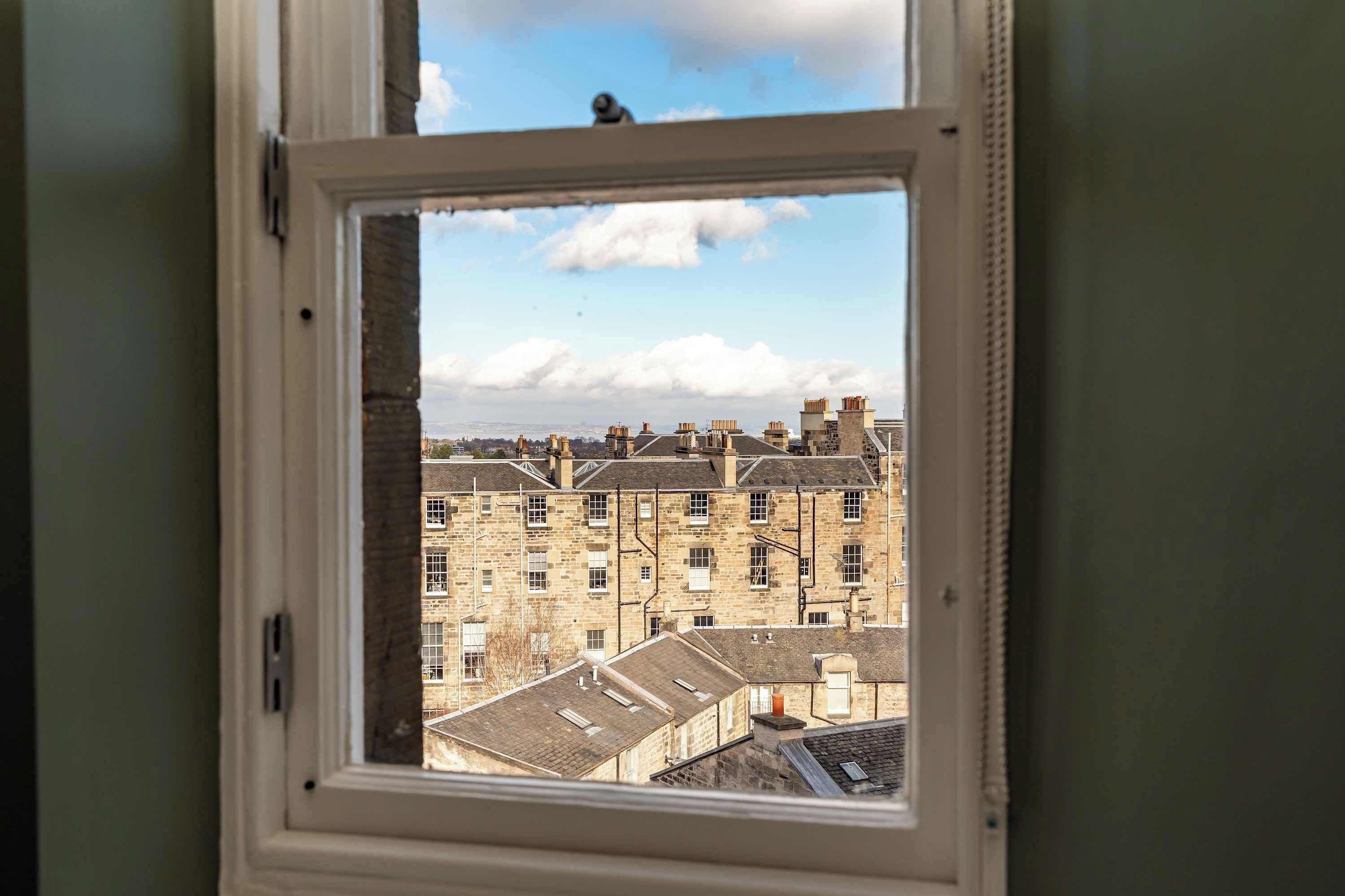 A window with a view of a row of stone buildings, some with chimneys.