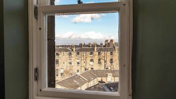 A window with a view of a row of stone buildings, some with chimneys.