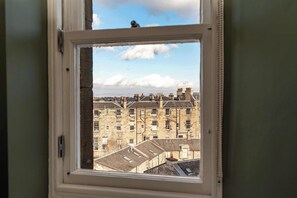 A window with a view of a row of stone buildings, some with chimneys. - Mackintosh Suite - 1 Bed Luxury Apartment (Edinburgh)