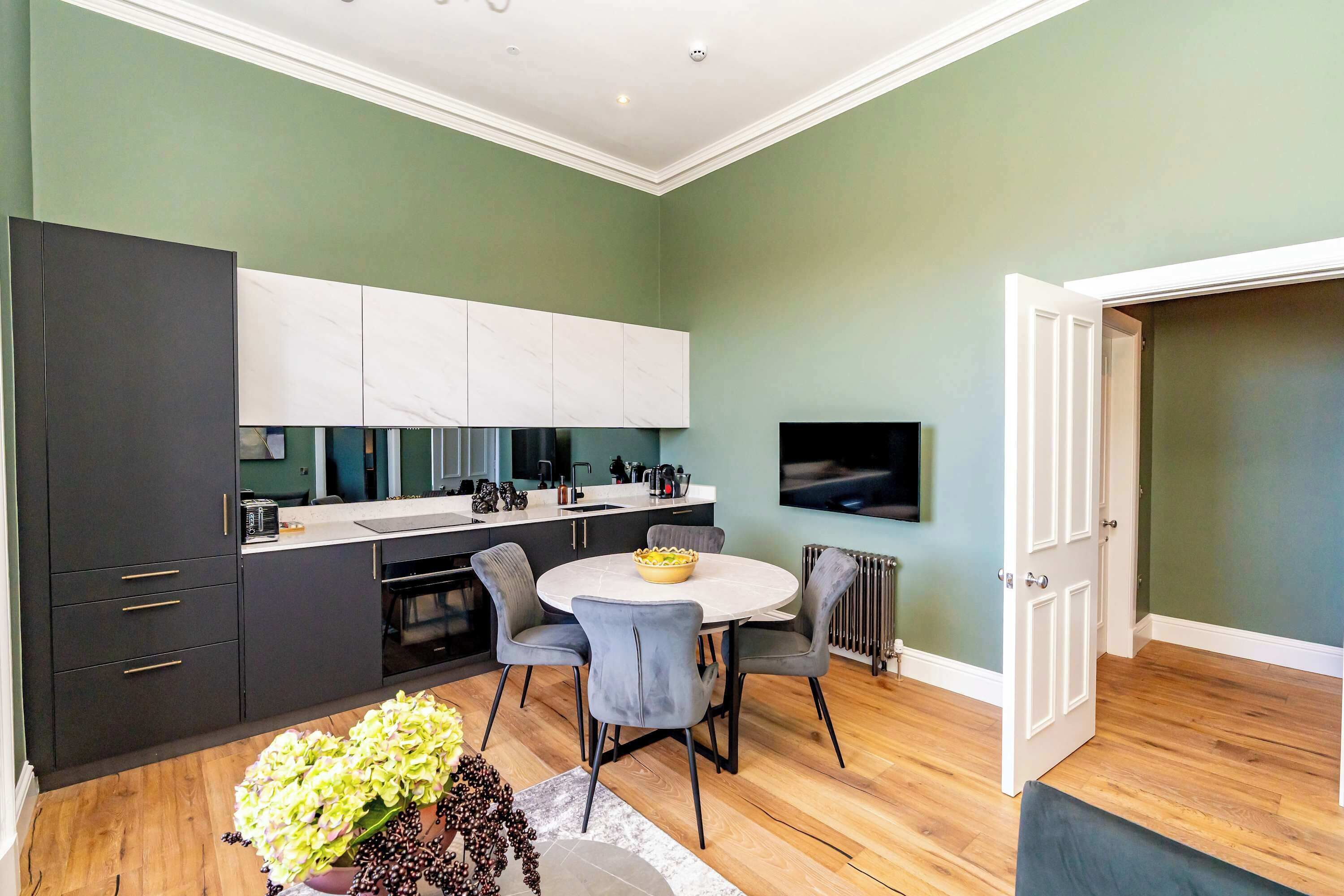 A modern kitchen with dark cabinetry, a white countertop, and a dining area with a round table and chairs.