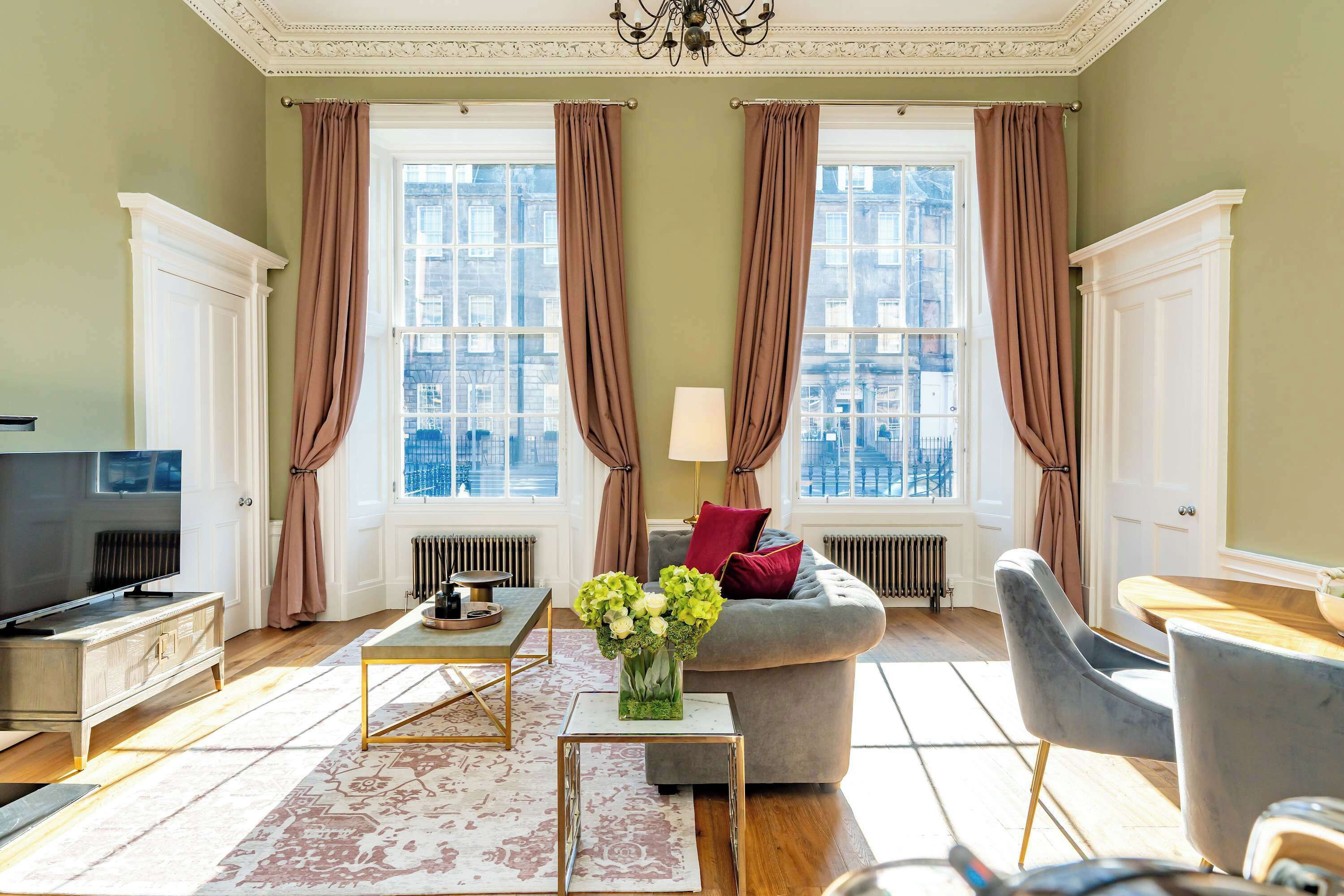 A well-lit living room with a television, sofa, coffee table, and a view of the city through large windows.