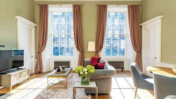 A well-lit living room with a television, sofa, coffee table, and a view of the city through large windows.