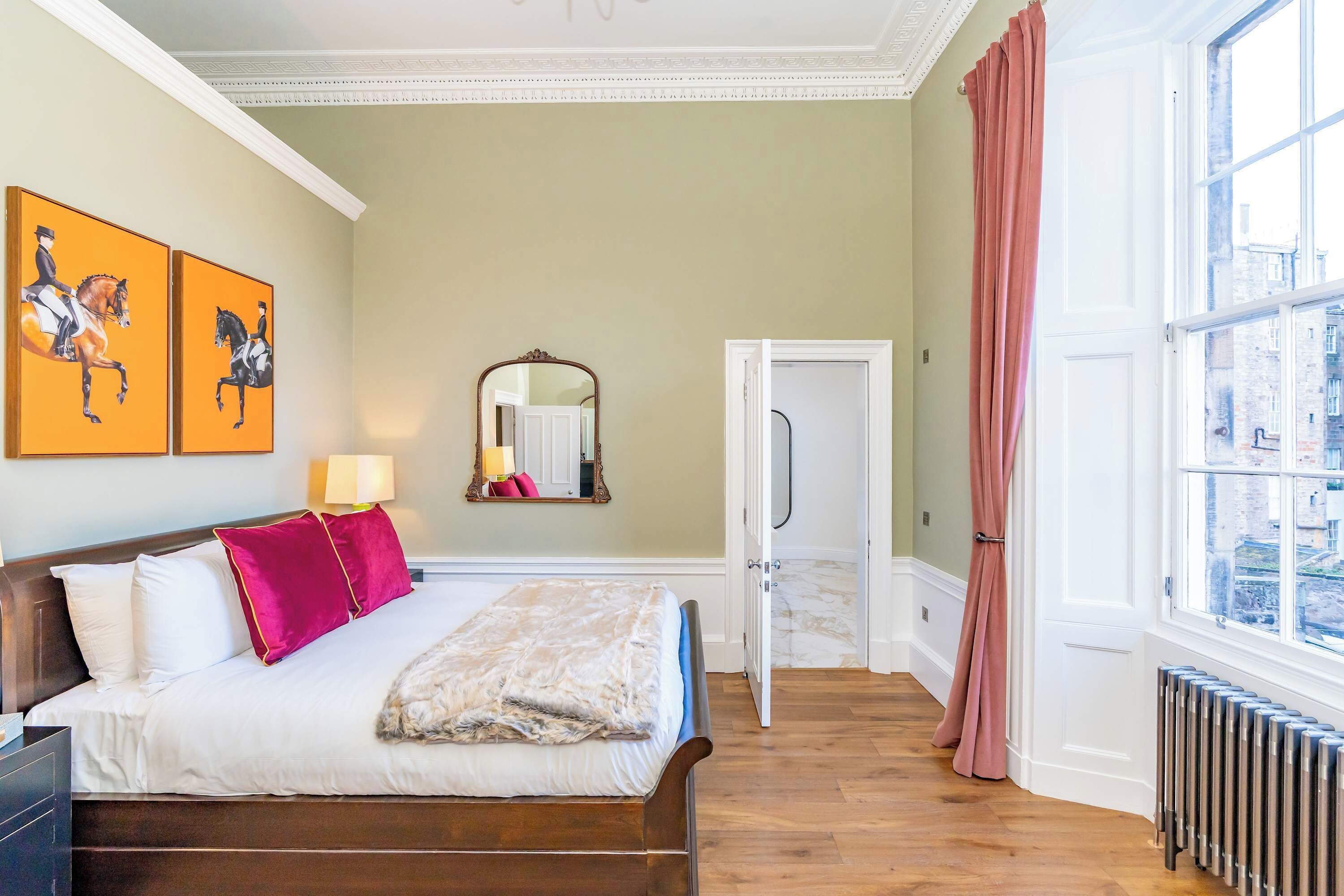 A hotel room with a bed, a mirror, a door, and a window with curtains.