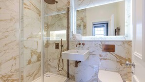 Un baño moderno con ducha envuelta en vidrio, un lavamanos blanco y un inodoro.