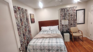 A bedroom with a bed, a chair, a nightstand, a lamp, and a painting on the wall.