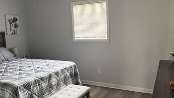 A bedroom with a bed, a bench, a ceiling fan, a window with blinds, and a nightstand.