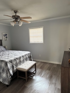 A bedroom with a bed, a bench, a ceiling fan, a window with blinds, and a nightstand.