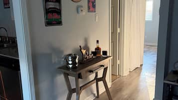 A hallway with a wooden floor, a table with a bottle and glasses, and wall decorations including a sign that says 'Fan Cave'.