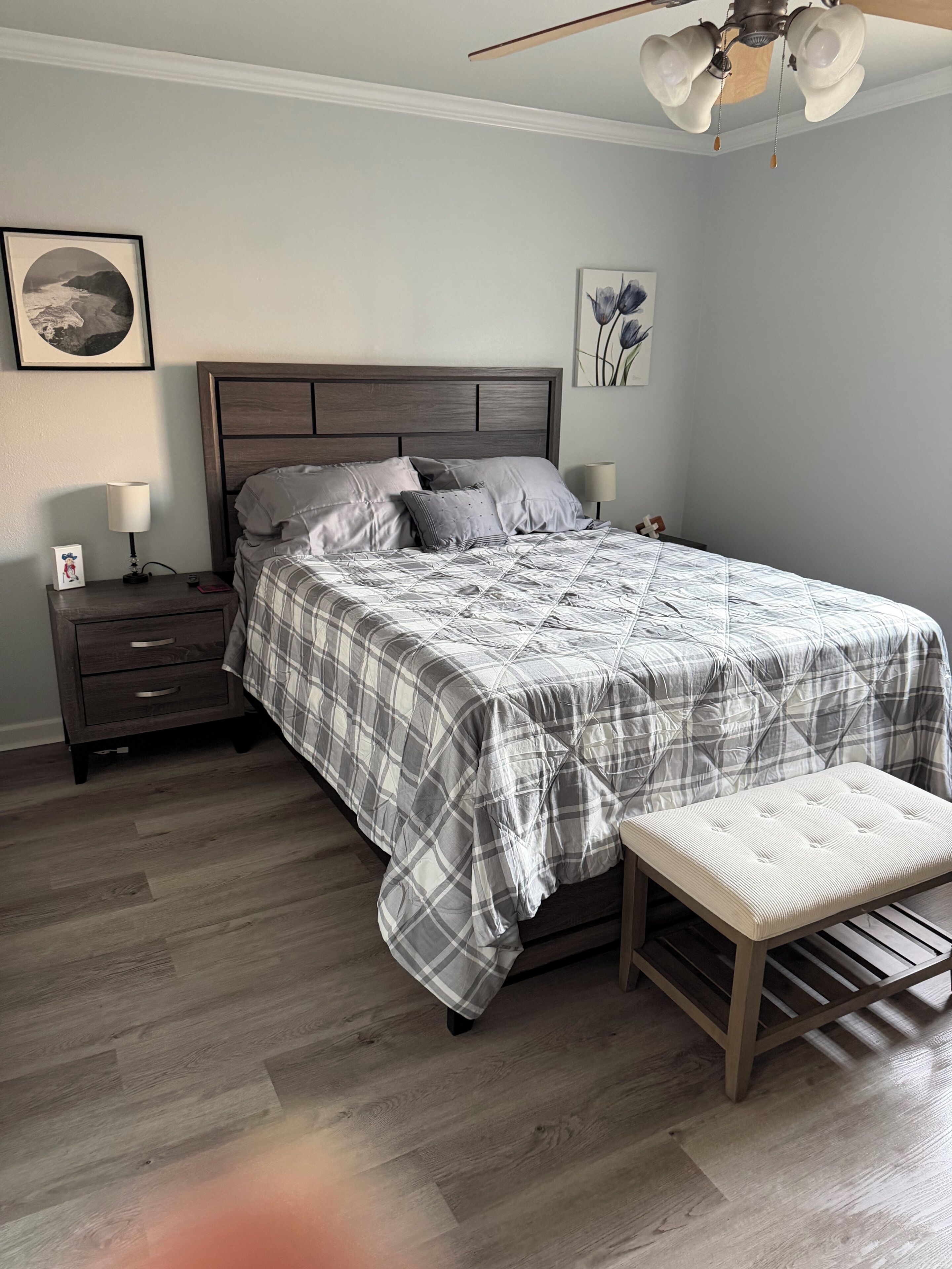 A bedroom with a bed, nightstands, a bench, a ceiling fan, and artwork on the walls.