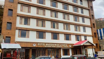 Hotel de vários andares com placa indicando 'Hotel Maheshwari Avenue', oferecendo restaurante, quartos e salões de festas.