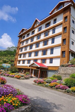 Ein mehrstöckiges Hotel mit einem zentralen Eingang, umgeben von bunten Blumenbeeten.