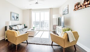 A modern living room with a sofa, two armchairs, a coffee table, a TV, and a balcony with a view. - Skyline-View Townhome | Sleeps 8 | Close to downtown, Broadway (Nashville)