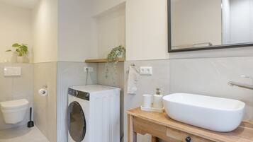 A modern bathroom with a toilet, washing machine, and a large sink.