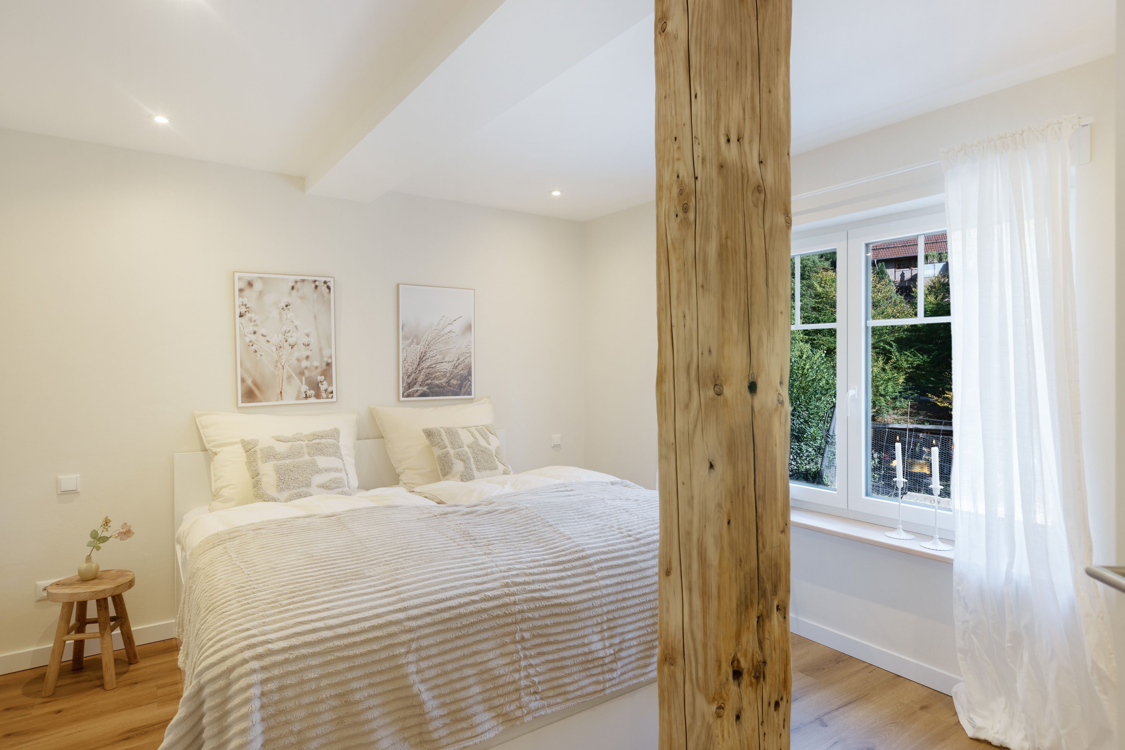 A bedroom with a large bed, two wall-mounted pictures, a wooden post, and a window with curtains.