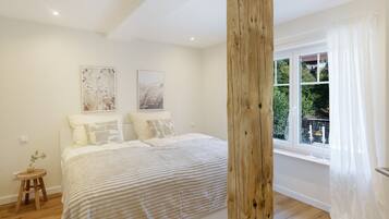 A bedroom with a large bed, two wall-mounted pictures, a wooden post, and a window with curtains.