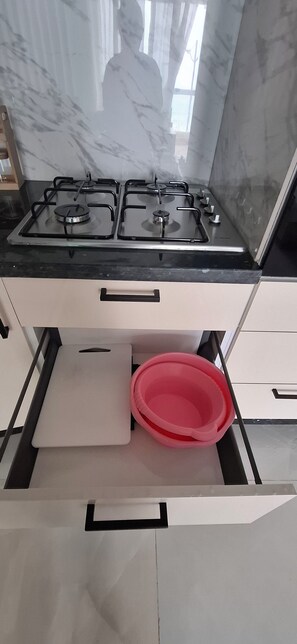 Una cocina con estufa a gas, un cajón con un recipiente rosa y salpicadero de mármol.